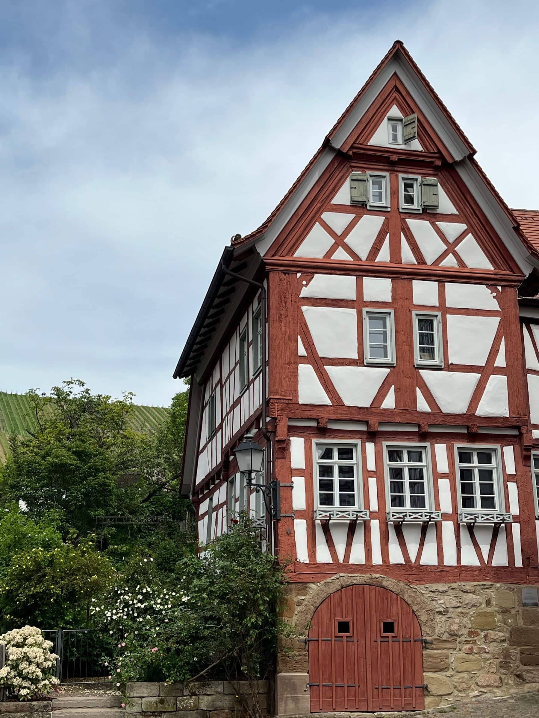 Fachwerkhaus mit rotbraunem Balkenwerk vor grünem Hang